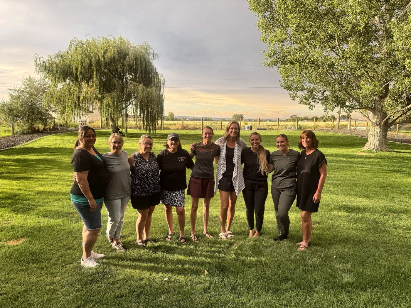 A group of Ugly Cry Club moms standing together on a lawn at sunset